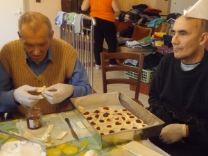 Uśmiechnięci pensjonatiusze wraz z personelem w czasie wypiekania smacznych ciasteczek w czapeczkach z papieru